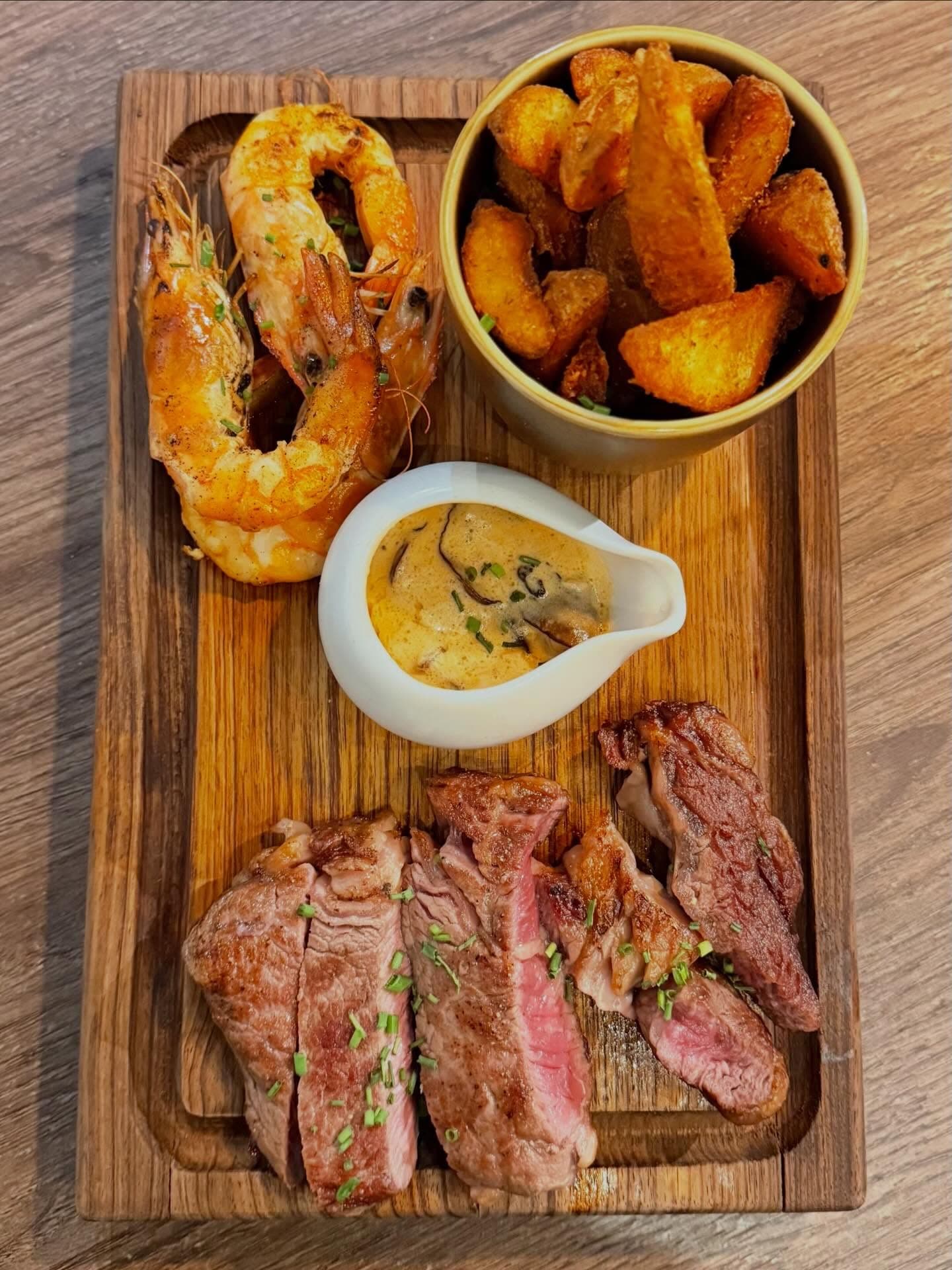 Surf & turf Artesão: sliced entrecôte, prawns, rustic fries and sauce on an oak board