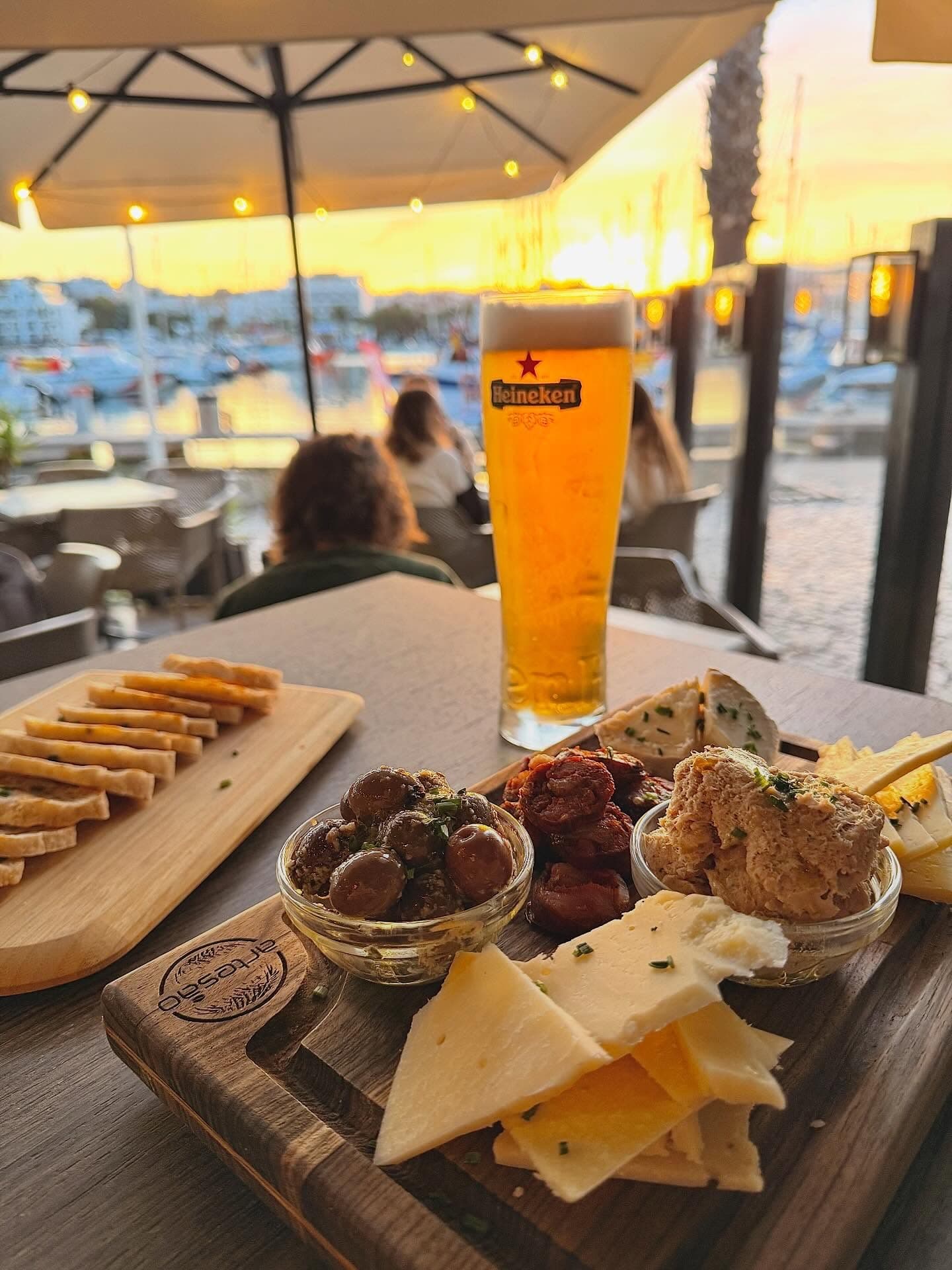 A beer and a tapas board on the terrace at sunset, boats in the marina behind